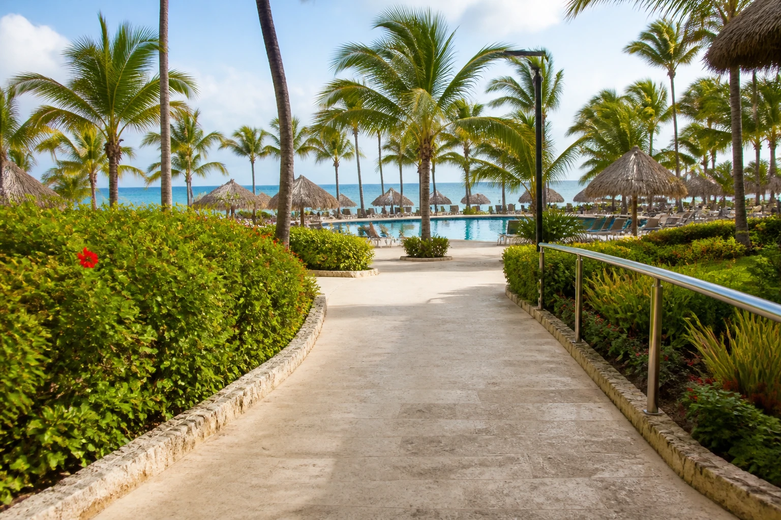 Accessible-looking resort pathway near a tropical pool and beach