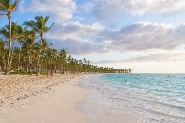 Punta Cana beach with pale sand, palms, turquoise water, and soft morning clouds